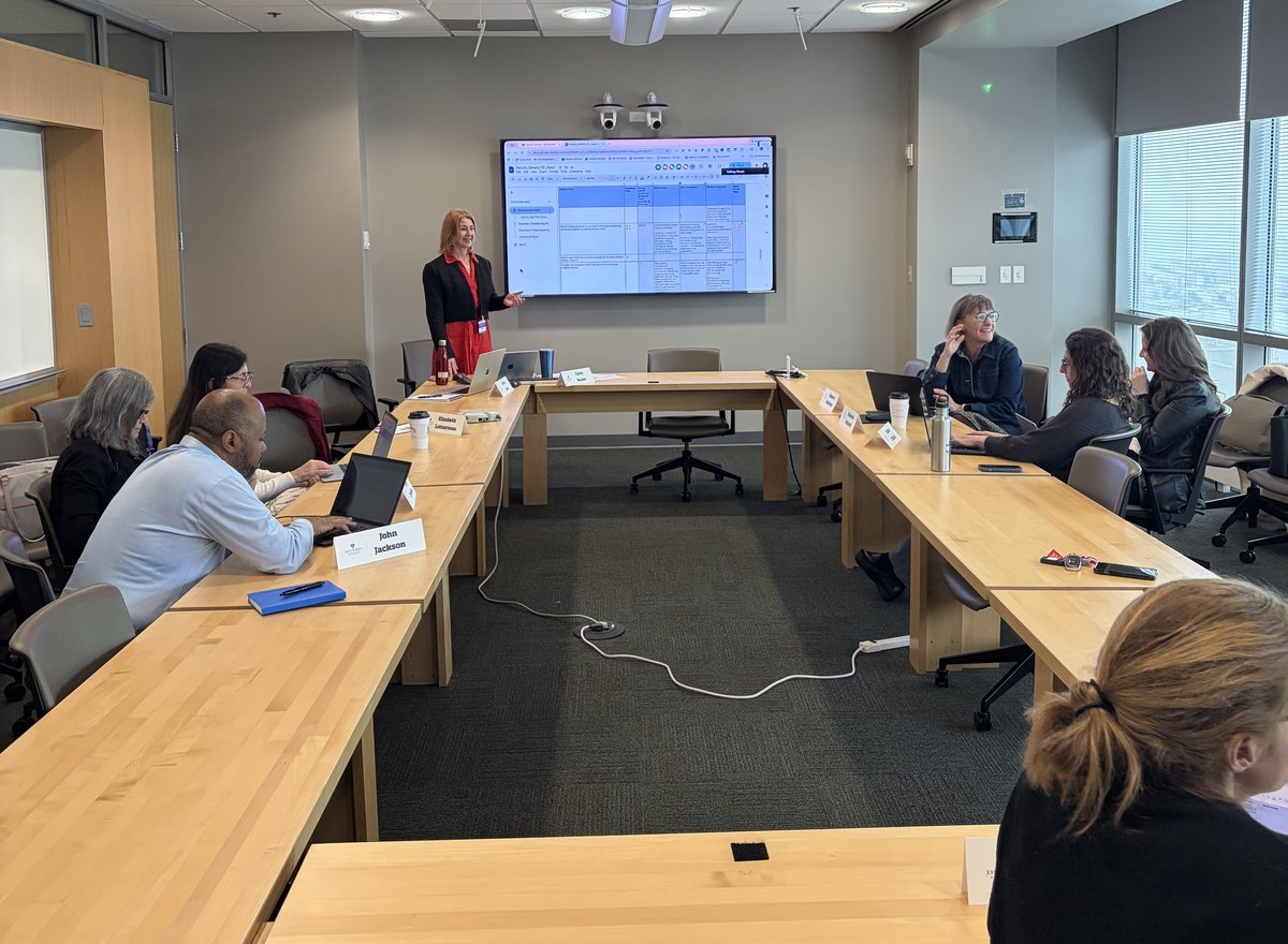 Cathy Becker facilitating a boardroom-style stakeholder meeting, presenting at a screen with participants seated around the table